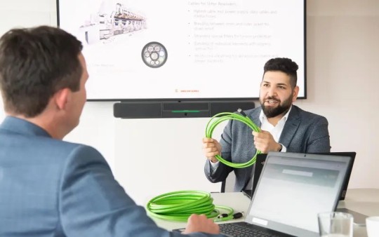 A Helukabel expert is holding a coil of a green cable and describing its use and benefits to a customer.