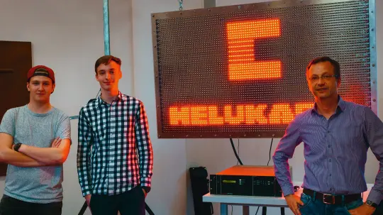 zwei Schüler und ihr Lehrer vor der LED Wand