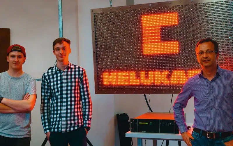 three men in front of a light wall with the red-glowing lettering HELUKABEL