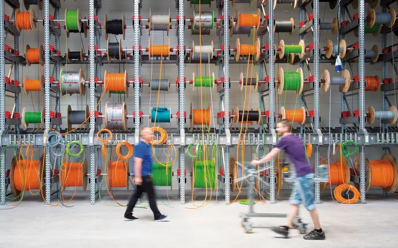 Big shelf with many cable drums in it and two men walking by it