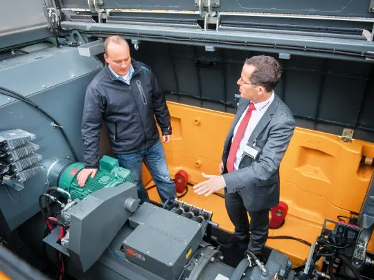 two men standing in the engine room of the excavator