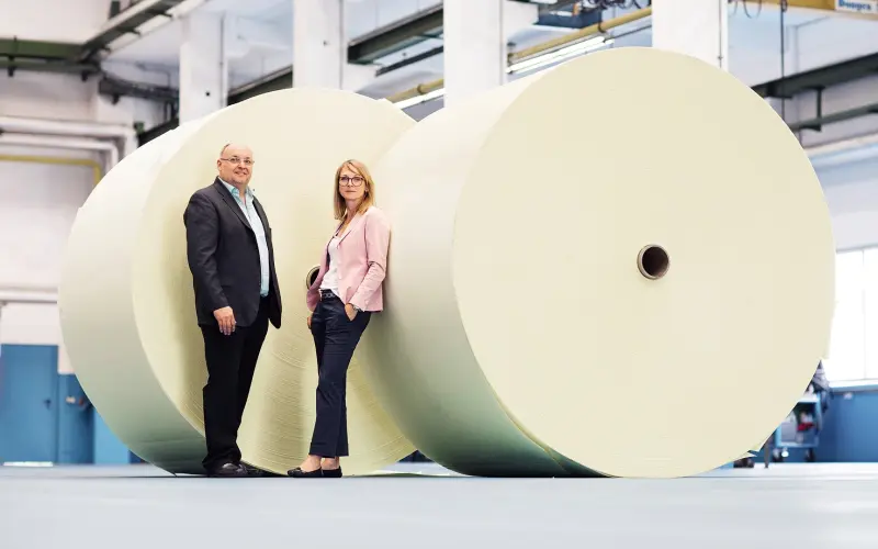Two persons standing in front of big wrapped rolls